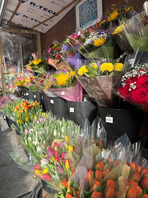 A variety of fresh flower bouquets arranged in black buckets inside a flower shop, featuring brightly colored blooms such as yellow daisies, purple lilacs, red roses, pink tulips, and orange tulips, a